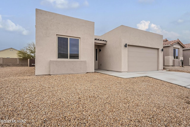 pueblo-style home with fence, an attached garage, stucco siding, concrete driveway, and a tiled roof