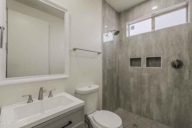 full bathroom with toilet, tiled shower, and vanity