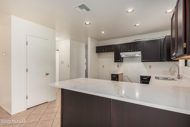 kitchen with visible vents, a sink, under cabinet range hood, a peninsula, and light stone countertops