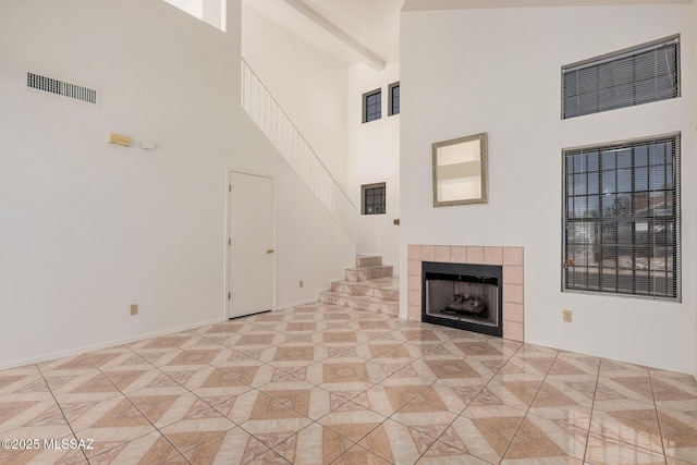 unfurnished living room featuring visible vents, a towering ceiling, a fireplace, and stairway