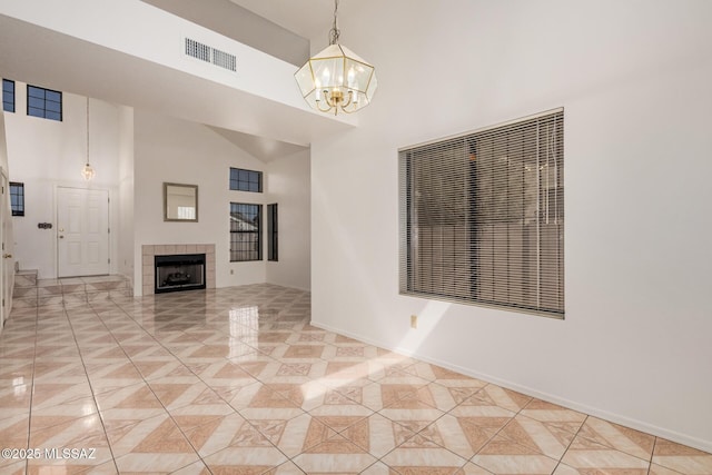 interior space featuring baseboards, visible vents, a high ceiling, a tile fireplace, and a chandelier