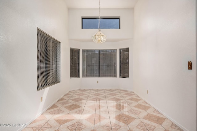 unfurnished room featuring a high ceiling, a notable chandelier, and baseboards