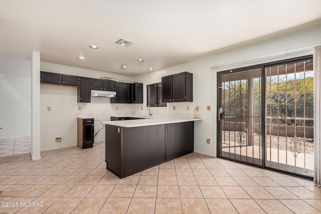 kitchen featuring visible vents, under cabinet range hood, light countertops, a peninsula, and a sink