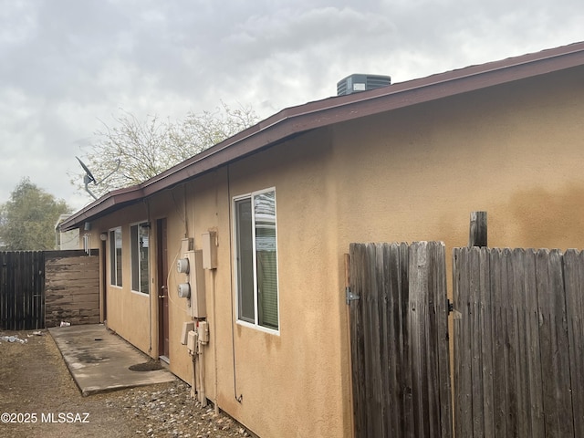 view of side of home featuring stucco siding, central AC unit, and fence