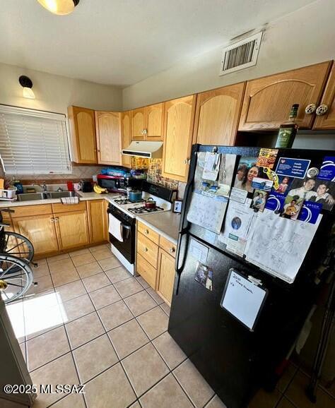 kitchen featuring visible vents, freestanding refrigerator, a sink, under cabinet range hood, and range with gas cooktop