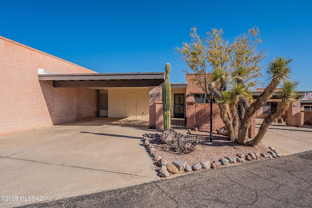 view of front facade featuring a carport, driveway, brick siding, and a gate