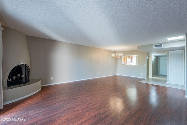 unfurnished living room with visible vents, a textured ceiling, wood finished floors, a fireplace, and a chandelier