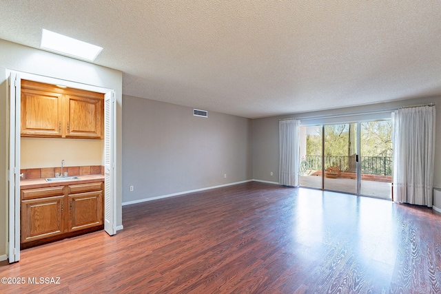 unfurnished living room featuring visible vents, a sink, a textured ceiling, wood finished floors, and baseboards