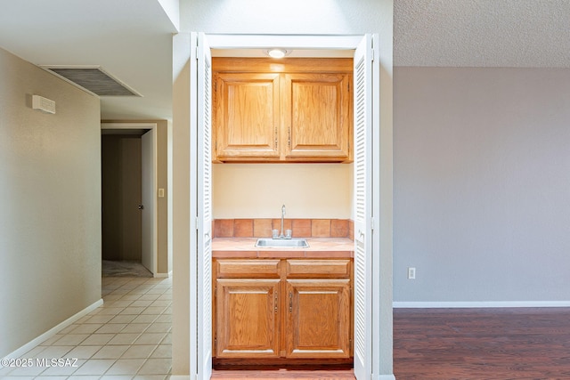 kitchen featuring baseboards, visible vents, light tile patterned flooring, a sink, and light countertops