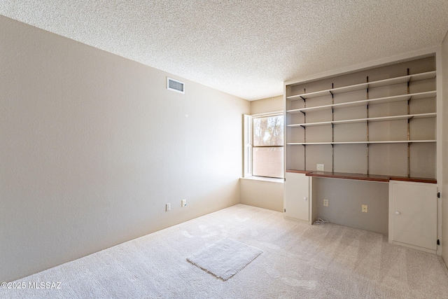 carpeted empty room featuring visible vents, a textured ceiling, and a textured wall