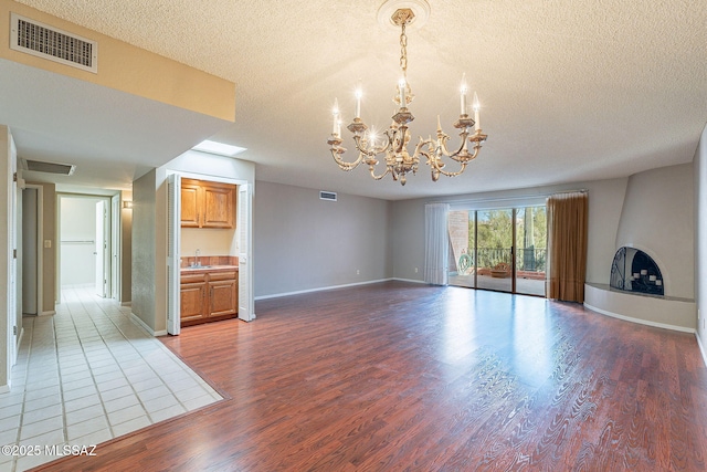 unfurnished living room featuring visible vents, a large fireplace, a textured ceiling, and wood finished floors