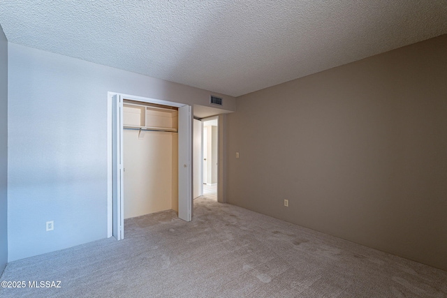 unfurnished bedroom featuring a closet, visible vents, light colored carpet, and a textured ceiling