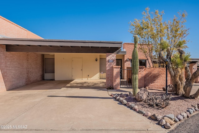 view of front of home featuring brick siding, fence, a carport, driveway, and a gate