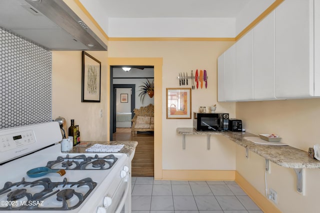 kitchen with black microwave, white gas stove, under cabinet range hood, light stone counters, and white cabinets