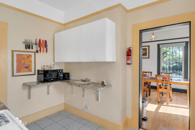 kitchen with a kitchen bar, light wood-style flooring, white cabinetry, baseboards, and light stone countertops