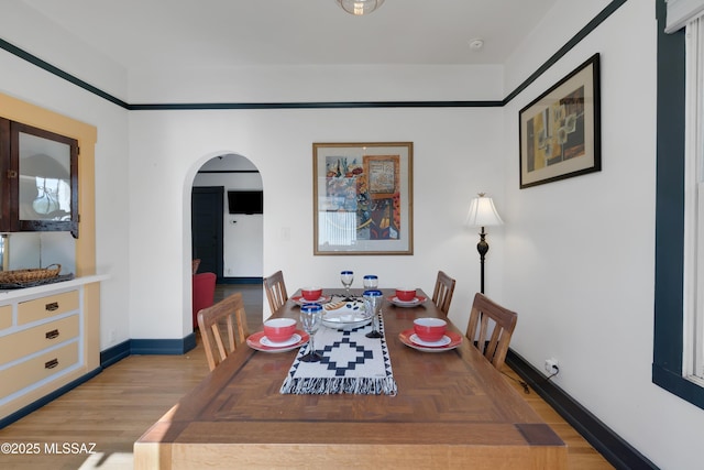 dining area with light wood-style floors, baseboards, and arched walkways