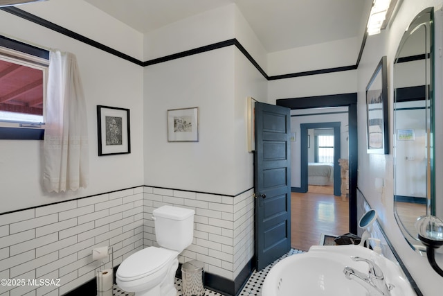 bathroom with wainscoting, tile walls, toilet, and a sink