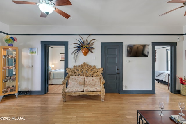 living area featuring a ceiling fan, light wood-style floors, and baseboards