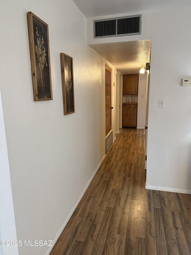 hall with a textured ceiling, dark wood-style floors, visible vents, and baseboards