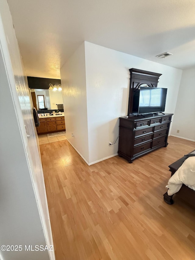 bedroom featuring visible vents, baseboards, light wood-type flooring, and ensuite bathroom