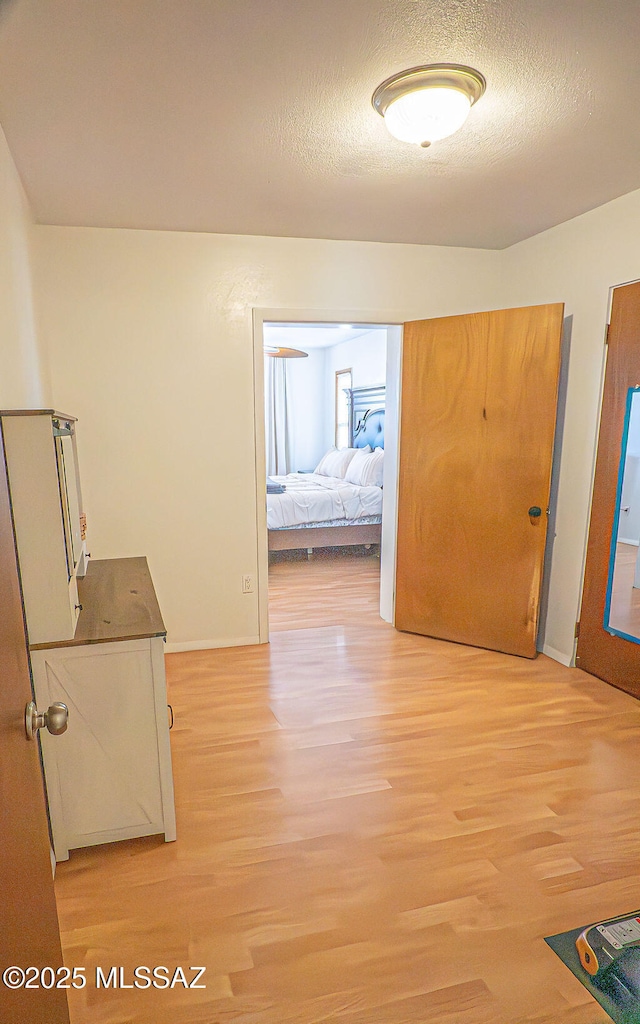 hall featuring light wood-style flooring, baseboards, and a textured ceiling