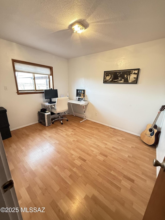 unfurnished office featuring light wood-style floors, baseboards, and a textured ceiling