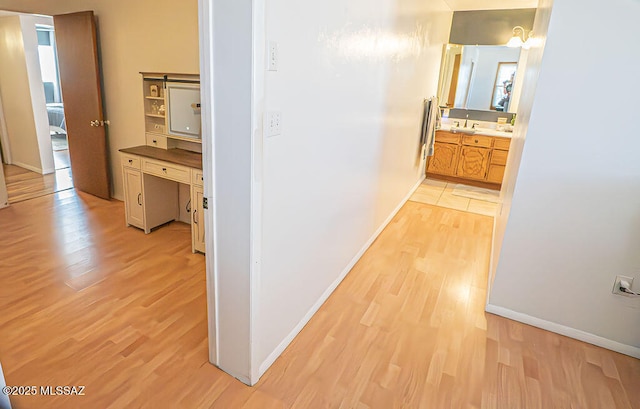 hall featuring a sink, light wood-style flooring, and baseboards