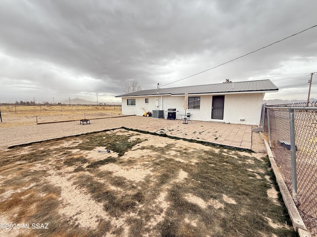 back of house featuring central AC, metal roof, fence, a patio, and stucco siding
