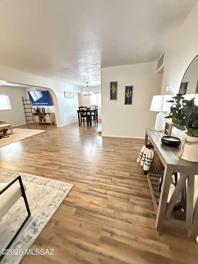 living area with arched walkways, a notable chandelier, wood finished floors, and a healthy amount of sunlight