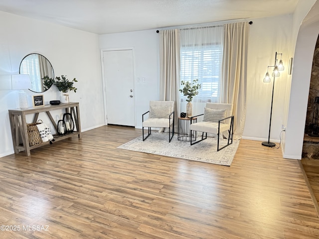 sitting room with arched walkways, baseboards, and wood finished floors