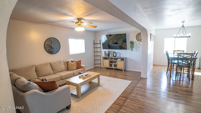living room with baseboards, arched walkways, wood finished floors, and ceiling fan with notable chandelier