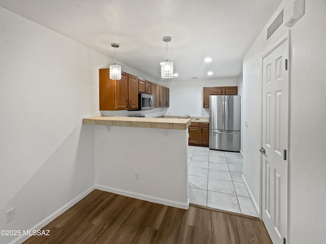 kitchen with stainless steel appliances, light wood-style floors, a peninsula, and light countertops