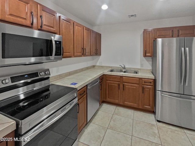 kitchen featuring stainless steel appliances, brown cabinets, visible vents, and tile counters