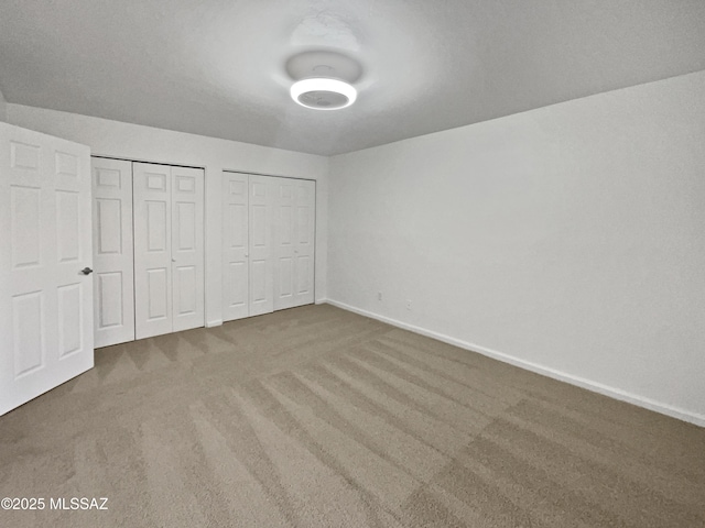 unfurnished bedroom with baseboards, carpet floors, and two closets