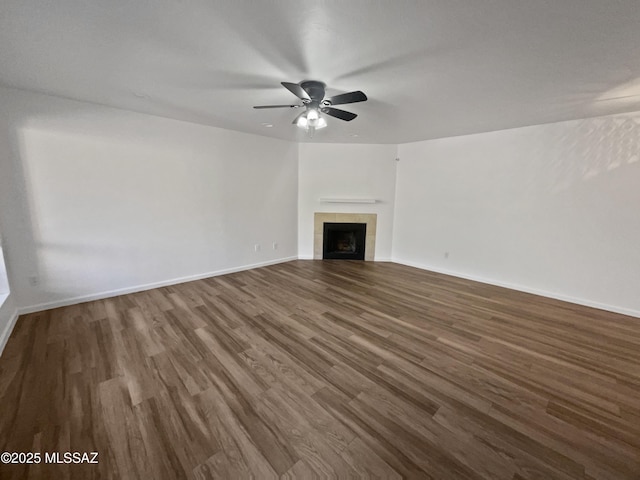 unfurnished living room with a tile fireplace, a ceiling fan, dark wood-type flooring, and baseboards