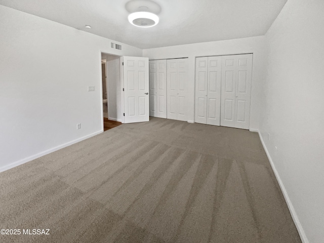 unfurnished bedroom with baseboards, visible vents, two closets, and carpet