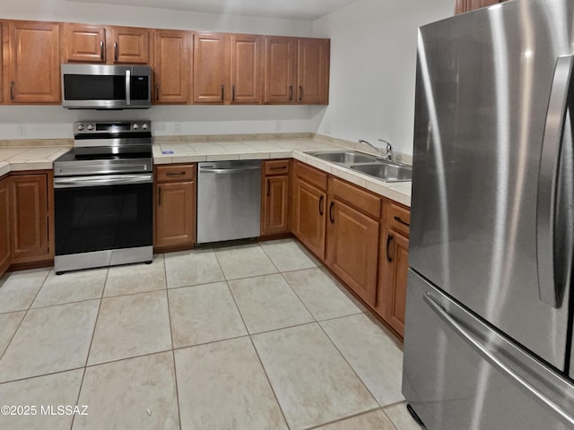 kitchen featuring a sink, tile counters, brown cabinets, and stainless steel appliances