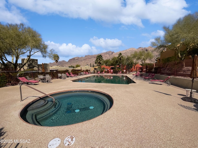 pool with a patio area, a mountain view, a community hot tub, and fence