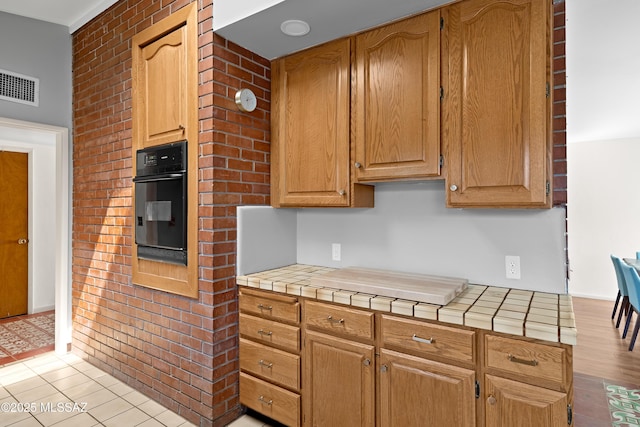 kitchen featuring brick wall, tile countertops, visible vents, and oven