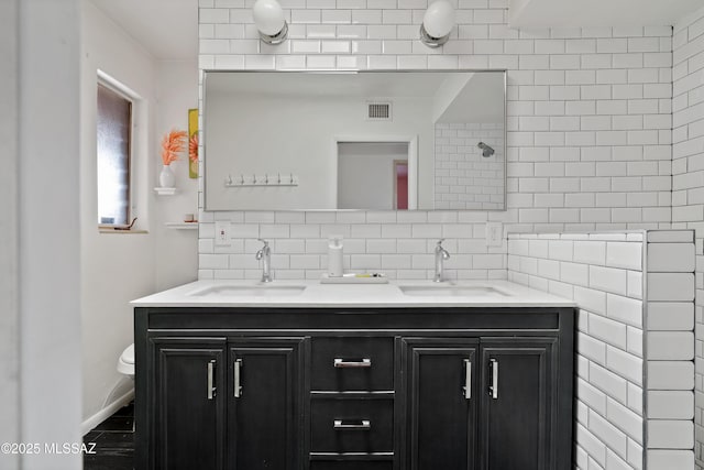 bathroom with toilet, double vanity, a sink, and visible vents