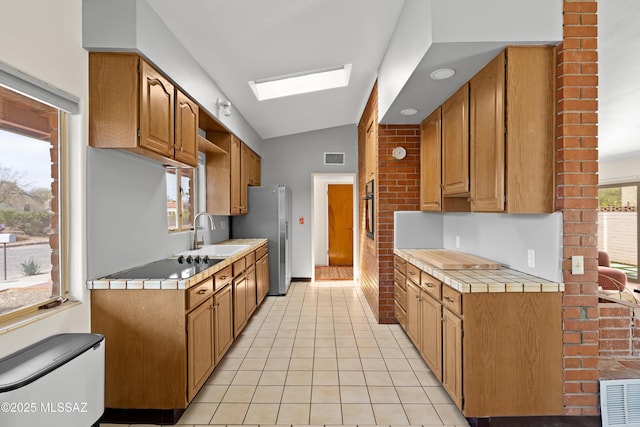 kitchen featuring freestanding refrigerator, visible vents, lofted ceiling with skylight, tile countertops, and a sink