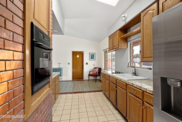 kitchen featuring stainless steel fridge with ice dispenser, dobule oven black, a sink, tile counters, and vaulted ceiling
