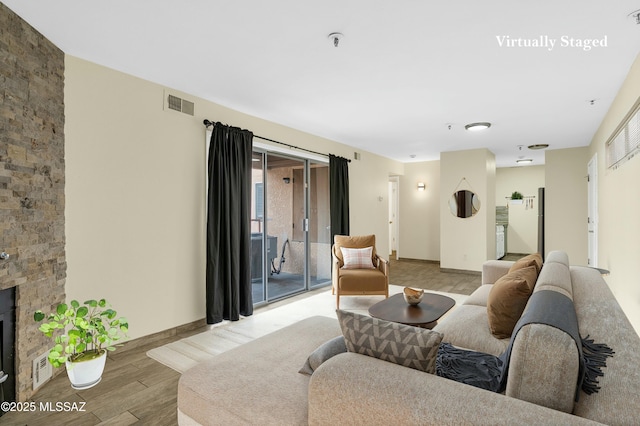 living area with light wood finished floors, visible vents, a stone fireplace, and baseboards