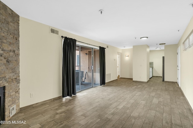 unfurnished living room with visible vents, baseboards, a stone fireplace, and wood finished floors