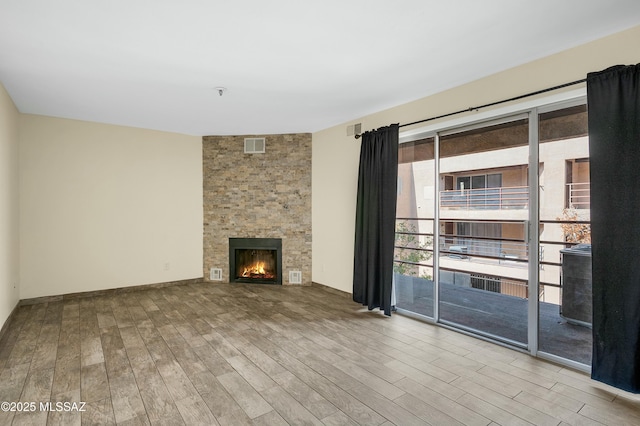 unfurnished living room featuring visible vents, a stone fireplace, and wood finished floors