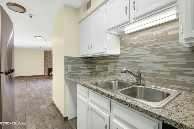 kitchen with a fireplace, freestanding refrigerator, a sink, white cabinets, and tasteful backsplash