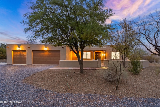 southwest-style home with gravel driveway, a garage, and stucco siding