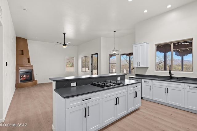 kitchen featuring light wood-style flooring, a fireplace, gas stovetop, a sink, and dark countertops