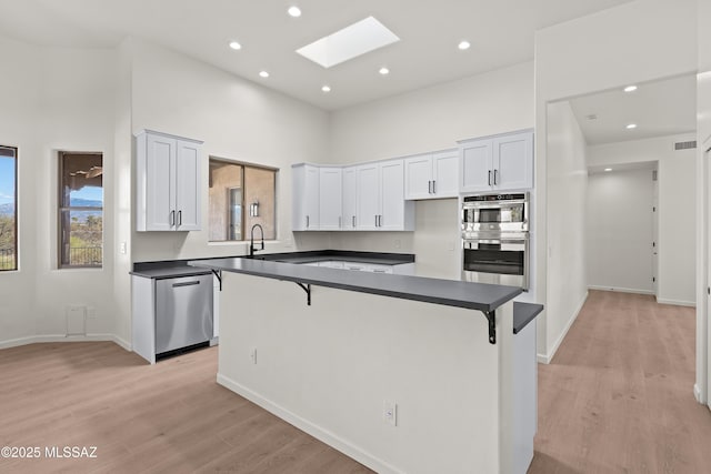 kitchen featuring dark countertops, appliances with stainless steel finishes, a skylight, and a kitchen breakfast bar