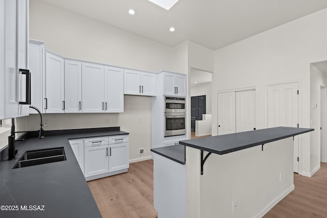 kitchen featuring light wood-style flooring, recessed lighting, a sink, white cabinetry, and dark countertops